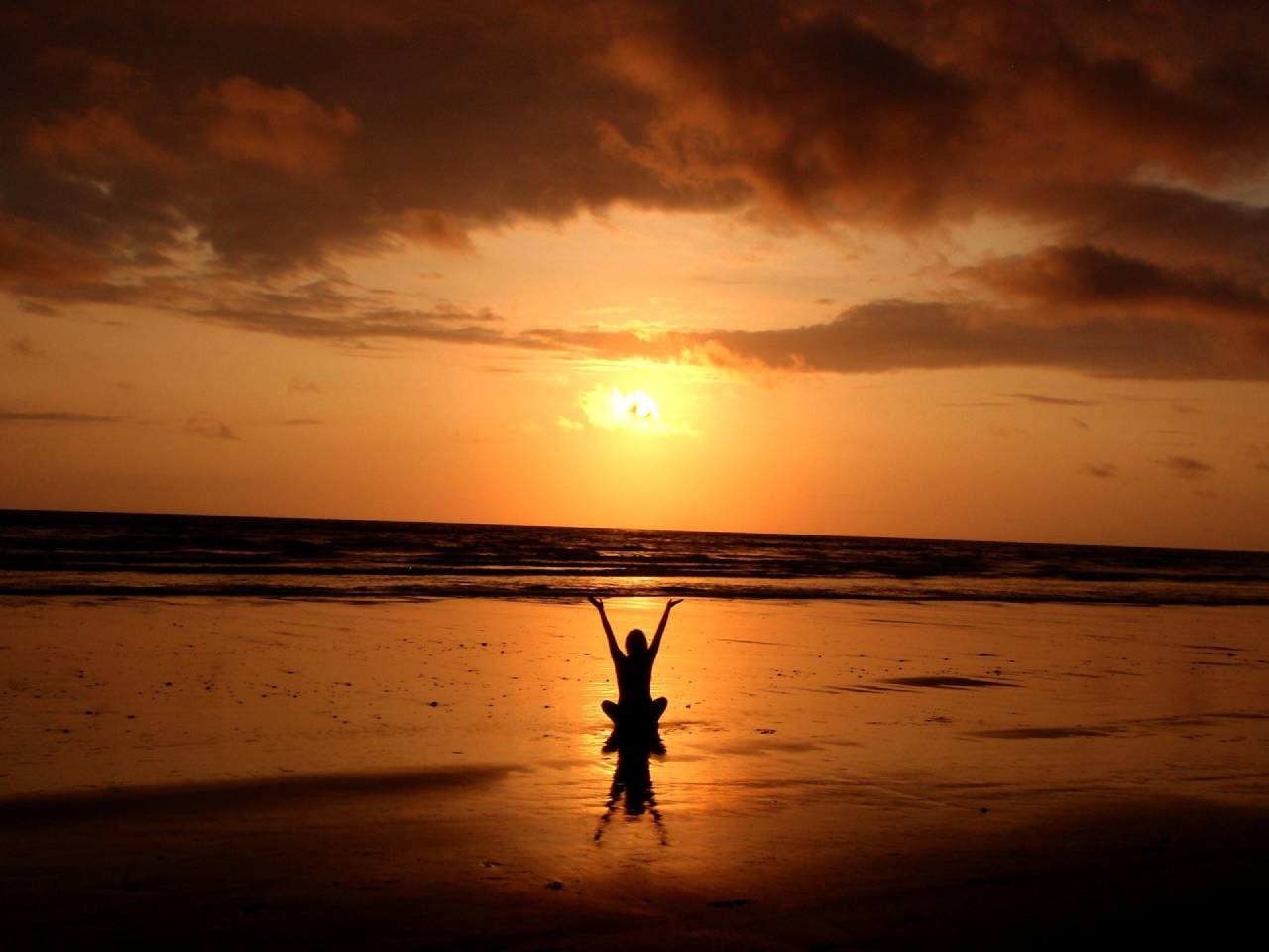 person sat on the beach with arms in the air at sunset